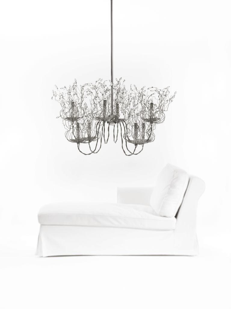 White chaise lounge beneath a decorative Spirits Chandelier Oval overhead