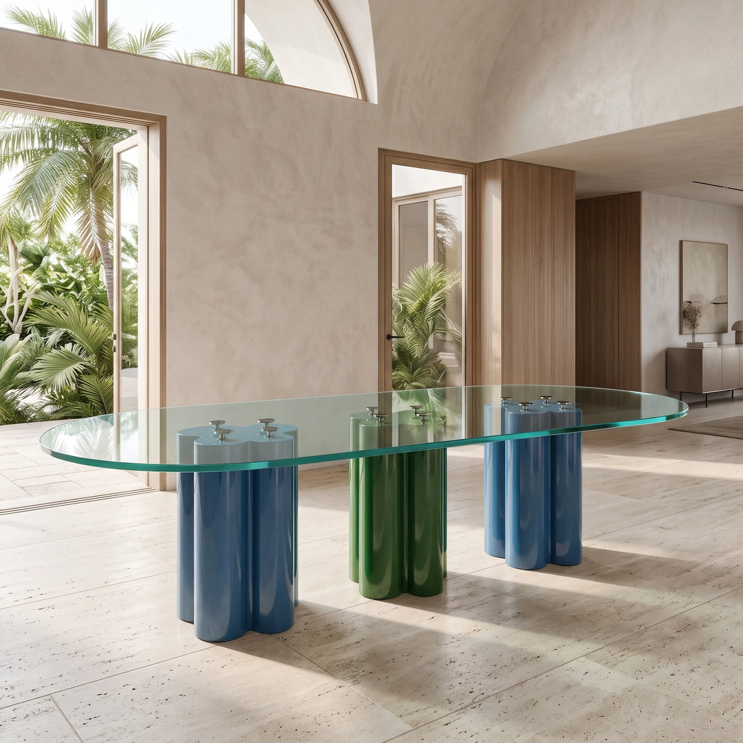 Sculptural Tripartite Glass Dining Table with an elongated rounded-end clear glass top supported by two blue and one central green cylindrical base groups in an architectural residential setting.